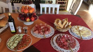 A table with various food items including fruits, cheeses, and bread, with a bottle of olive oil and salt shakers. - Agriturismo Campallegro (Cecina)