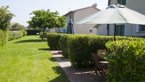 A well-maintained garden with a paved walkway, a bench, and a large umbrella providing shade. - Agriturismo Campallegro (Cecina)