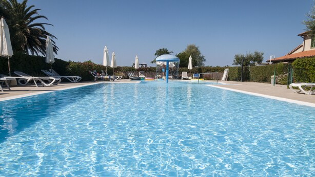 A clear swimming pool with lounge chairs and umbrellas, surrounded by greenery and a building. - Agriturismo Campallegro (Cecina)
