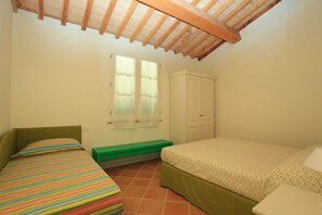 Un dormitorio con dos camas, una ventana con cortinas, un armario y un techo inclinado con vigas de madera.