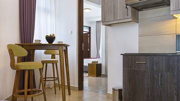 A compact kitchen with dark wood cabinets, a stainless steel range hood, and a small dining area with two stools and a table.