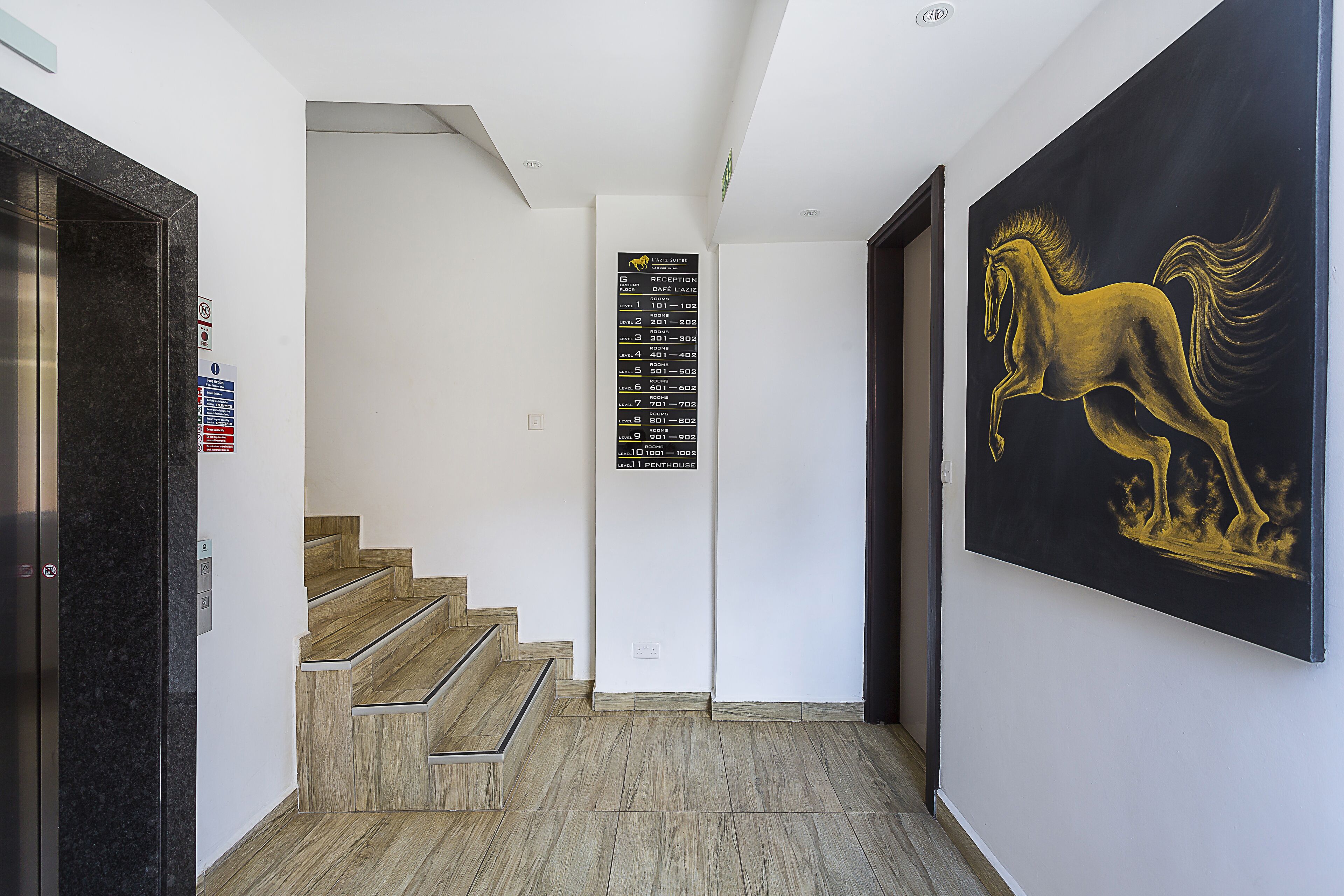 Un pasillo de hotel con una escalera, un letrero de recepción y un cuadro grande de un caballo.