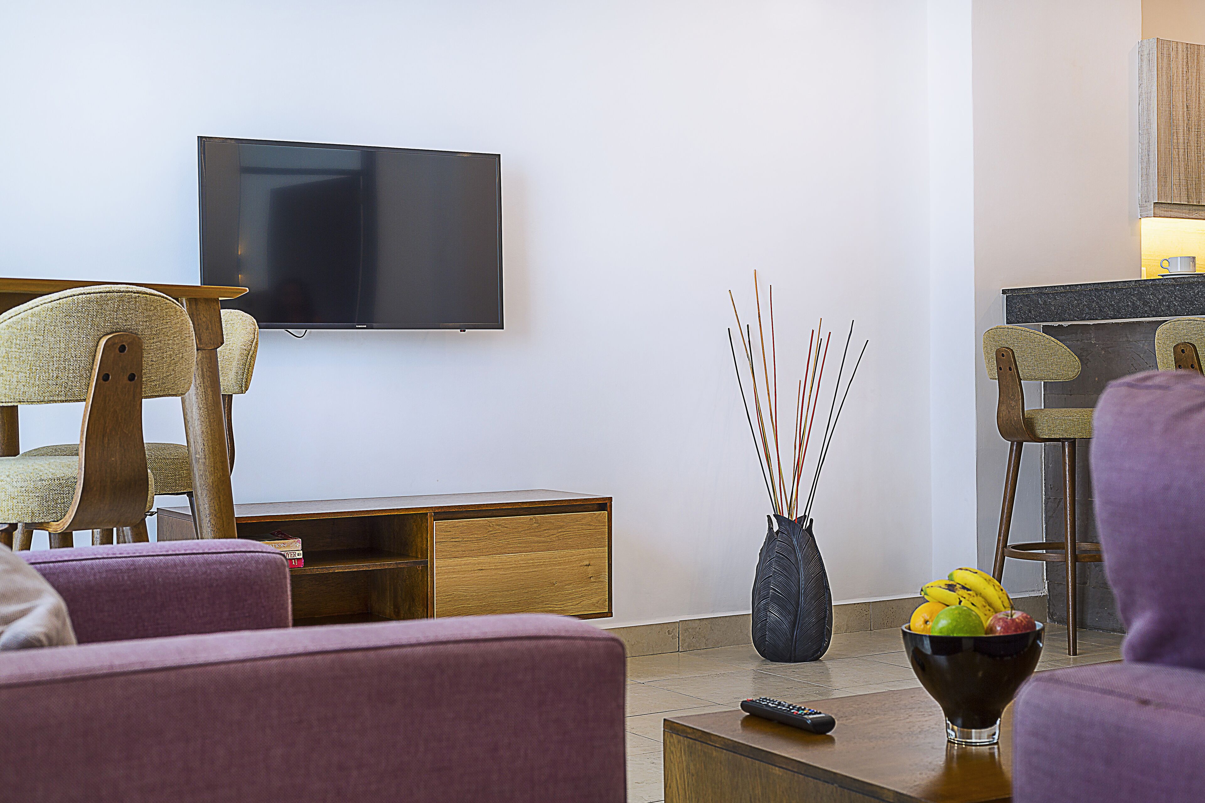 A modern living room with a flat-screen TV, wooden furniture, and a fruit bowl on a coffee table.