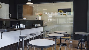 A modern cafe interior with a bar area, multiple round tables, and stools. - L'Aziz Suites (Nairobi)