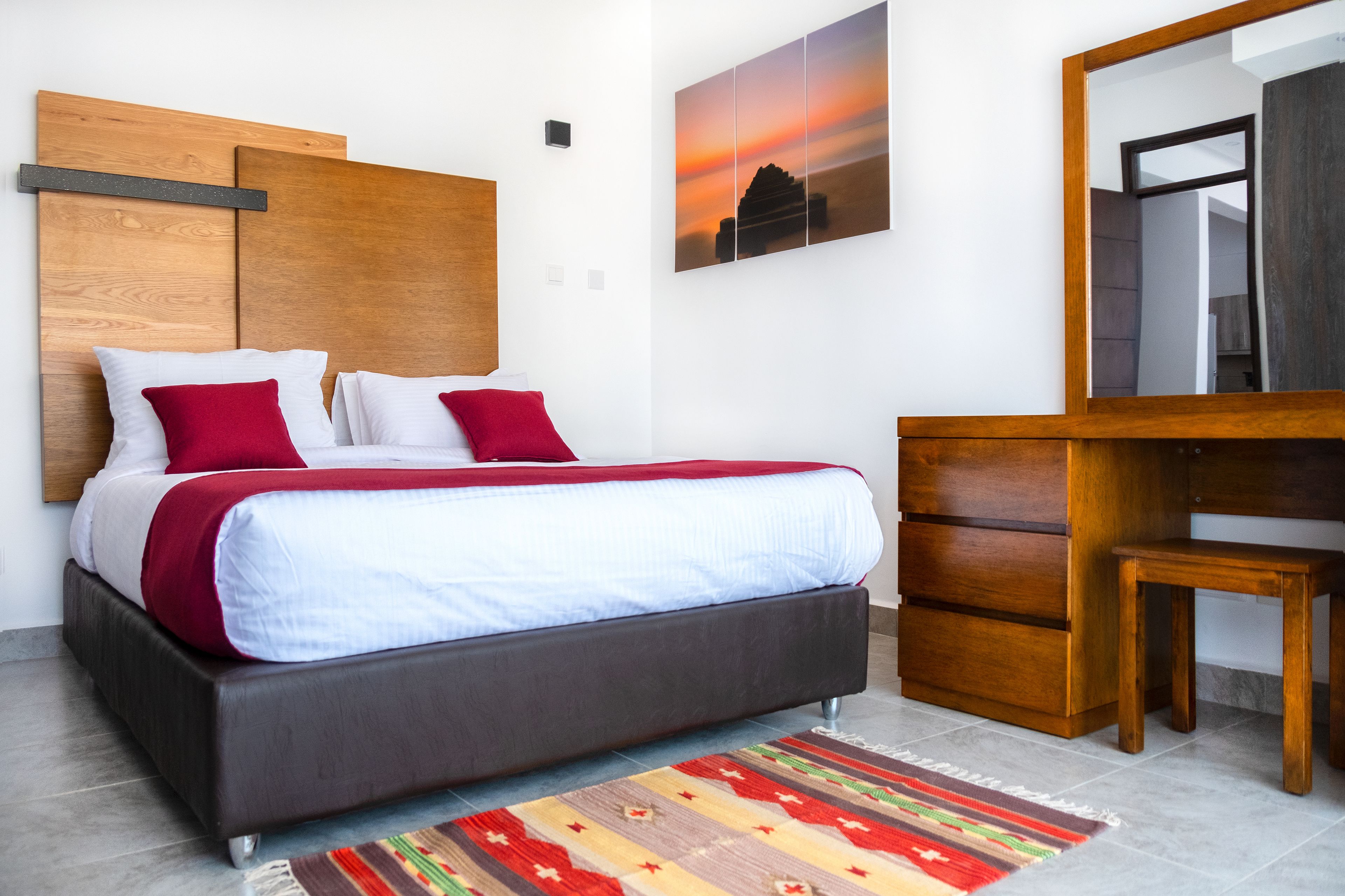 A modern bedroom with a bed, a wooden headboard, a nightstand, a dresser, and a large mirror.