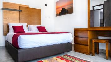 A modern bedroom with a bed, a wooden headboard, a nightstand, a dresser, and a large mirror.