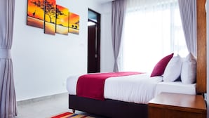 A modern hotel room with a bed, a wooden nightstand, a colorful striped rug, and a wall with three sunset paintings. - L'Aziz Suites (Nairobi)