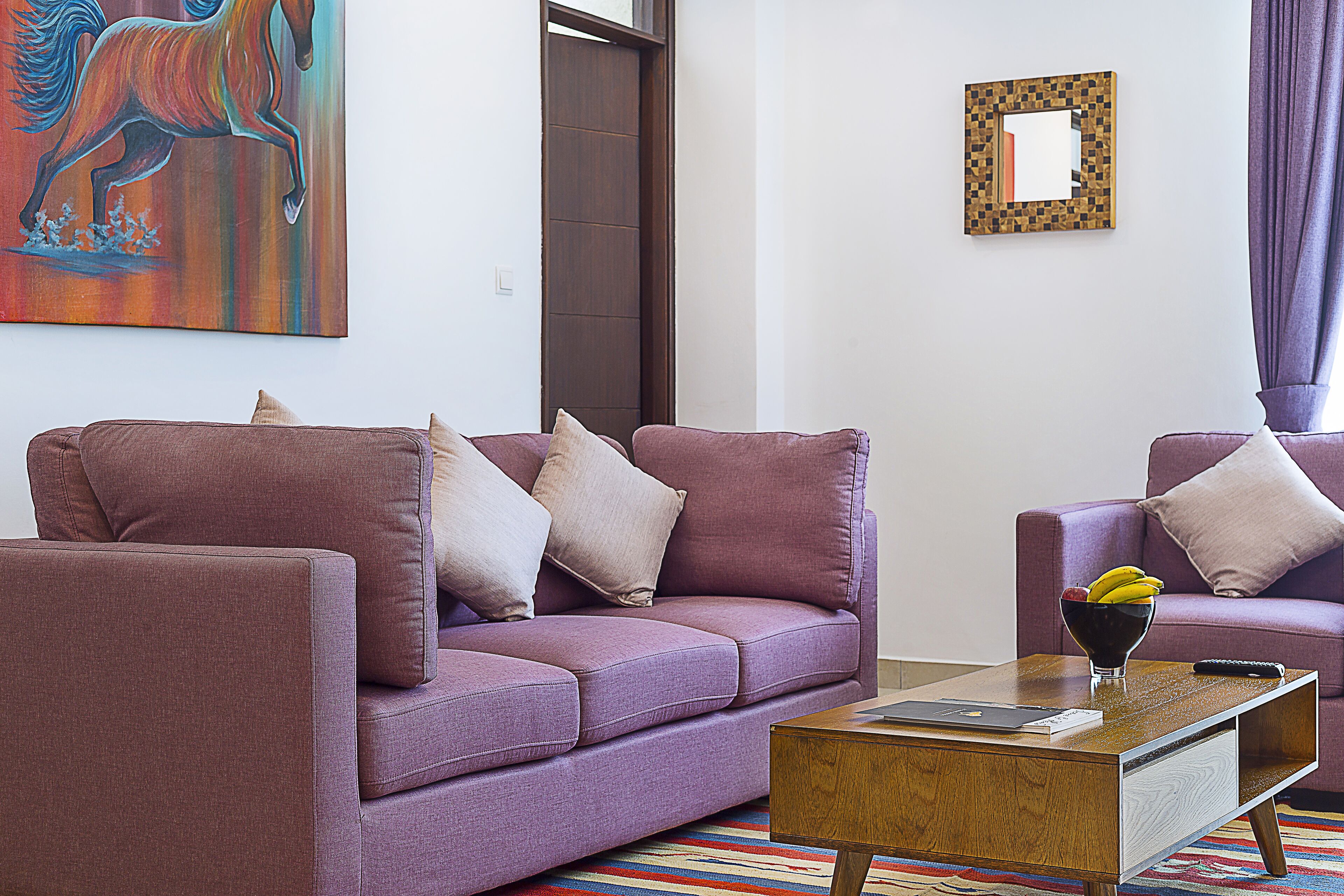 A living room with a purple sofa, a coffee table, and a painting of a horse.