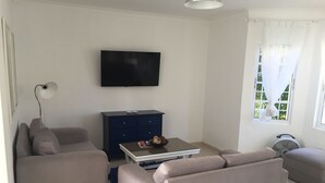 A modern living room with a flat-screen TV, a dark blue cabinet, a sofa, a coffee table, and a window with curtains. - Punta Cana Paradise 3 Bedroom Villa Close to Beach (Punta Cana)