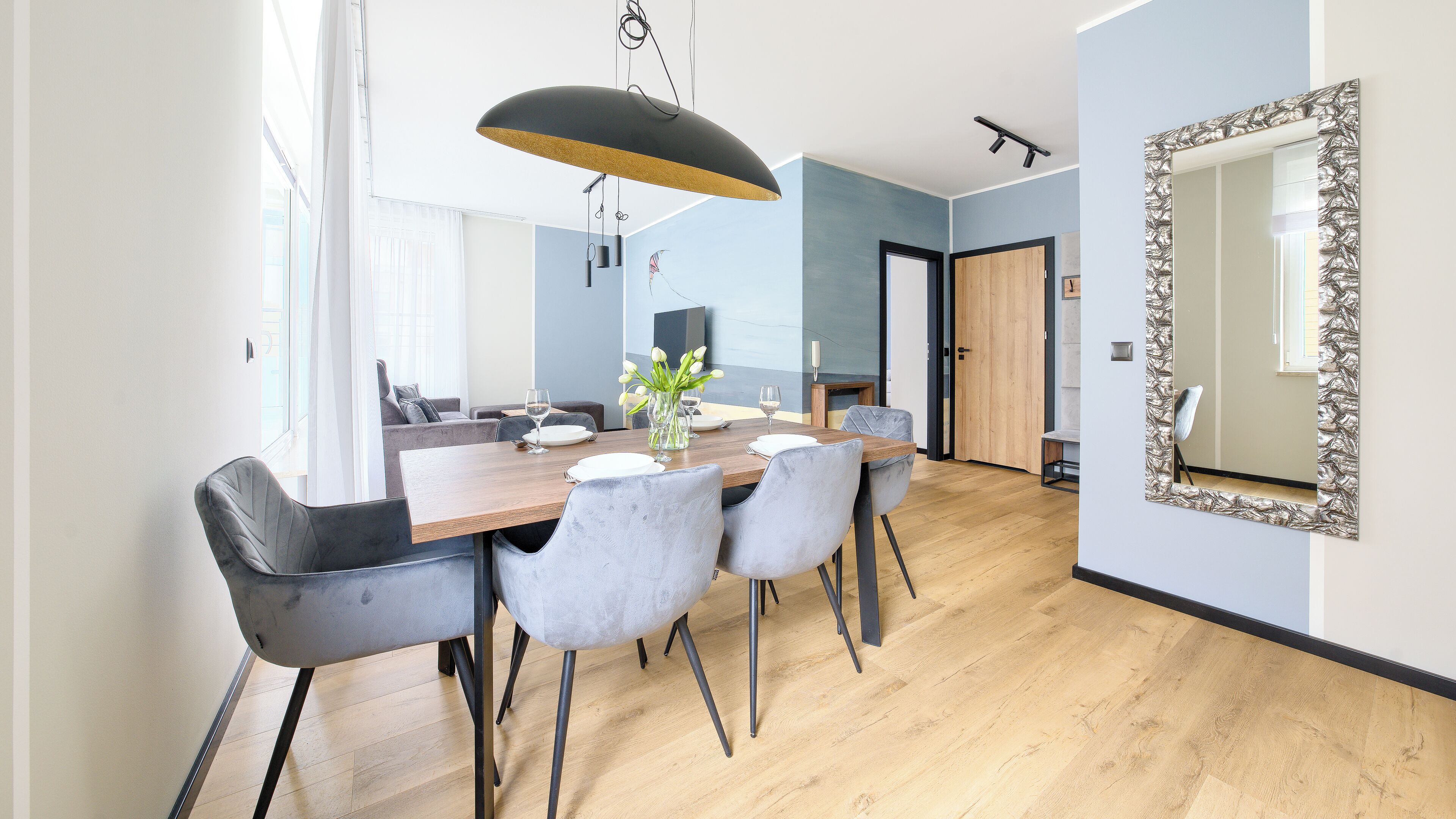 A modern dining area with a wooden table, grey upholstered chairs, and a pendant light.
