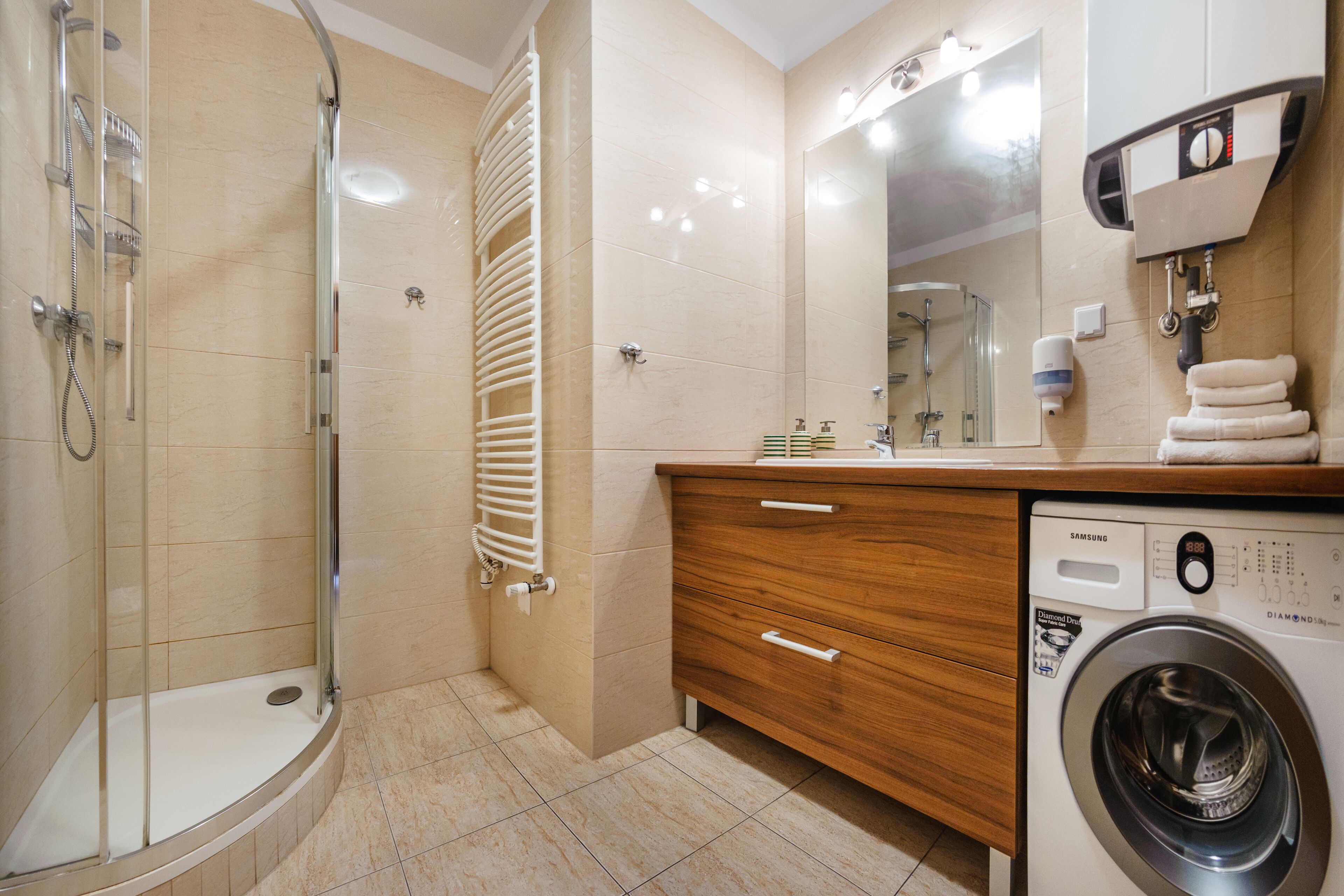 A modern bathroom with a glass shower enclosure, a built-in toilet, a wooden vanity with a washing machine, and a large mirror.