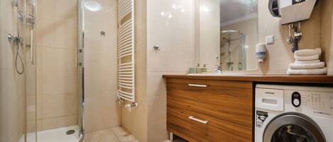 A modern bathroom with a glass shower enclosure, a built-in toilet, a wooden vanity with a washing machine, and a large mirror.