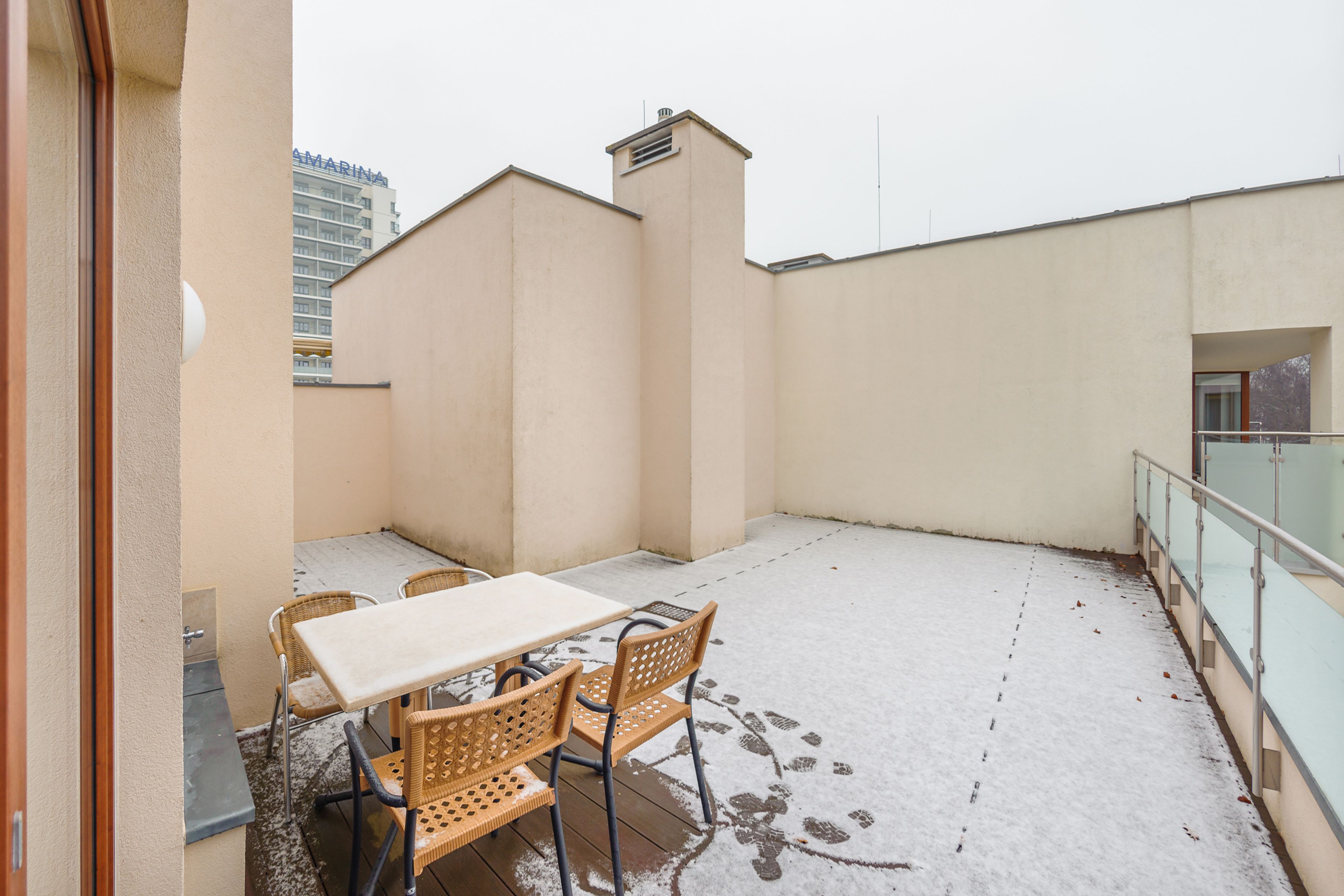 A balcony with a table and chairs, a glass railing, and a building in the background.