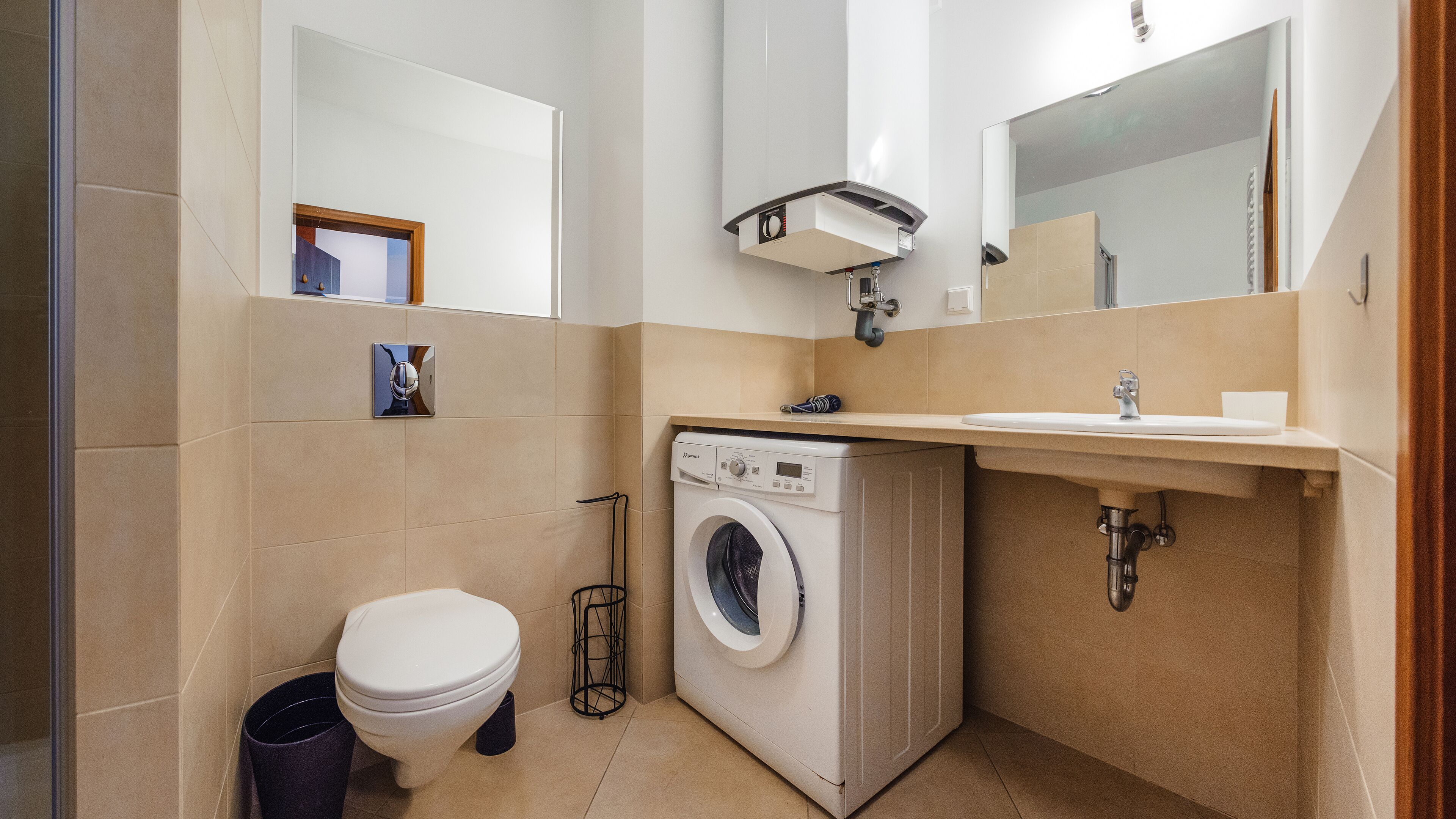 A compact bathroom with a toilet, washing machine, sink, and mirrors.
