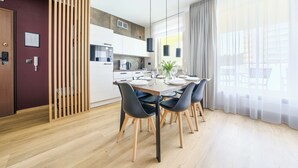A modern kitchen with white cabinets, a wooden floor, and a dining area with a table set for four. - Apartamenty Sun & Snow Aquamarina (Miedzyzdroje)