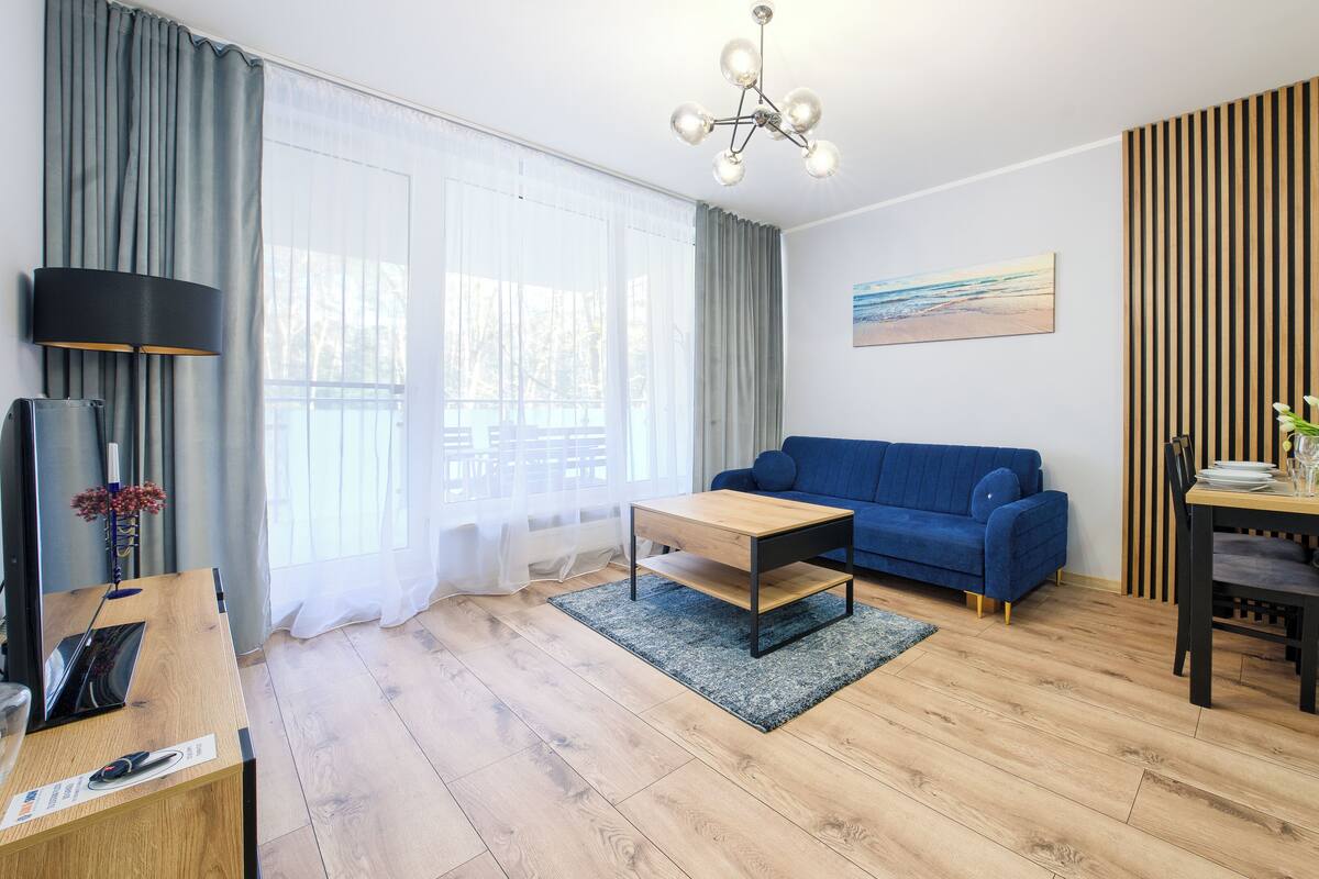 A modern living room with a blue sofa, wooden coffee table, and a dining area with a wooden table and chairs.
