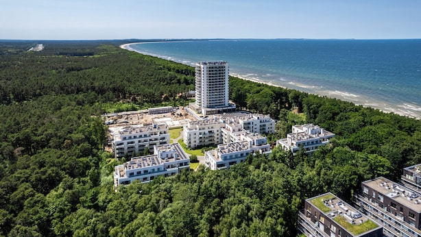 An aerial view of a coastal residential area with a high-rise building, multiple low-rise buildings, and a beach. - Apartamenty Sun & Snow Aquamarina (Miedzyzdroje)