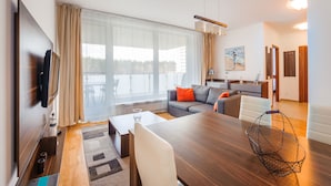 A modern living room with a wooden dining table, a sofa, and a TV mounted on the wall. - Apartamenty Sun & Snow Aquamarina (Miedzyzdroje)