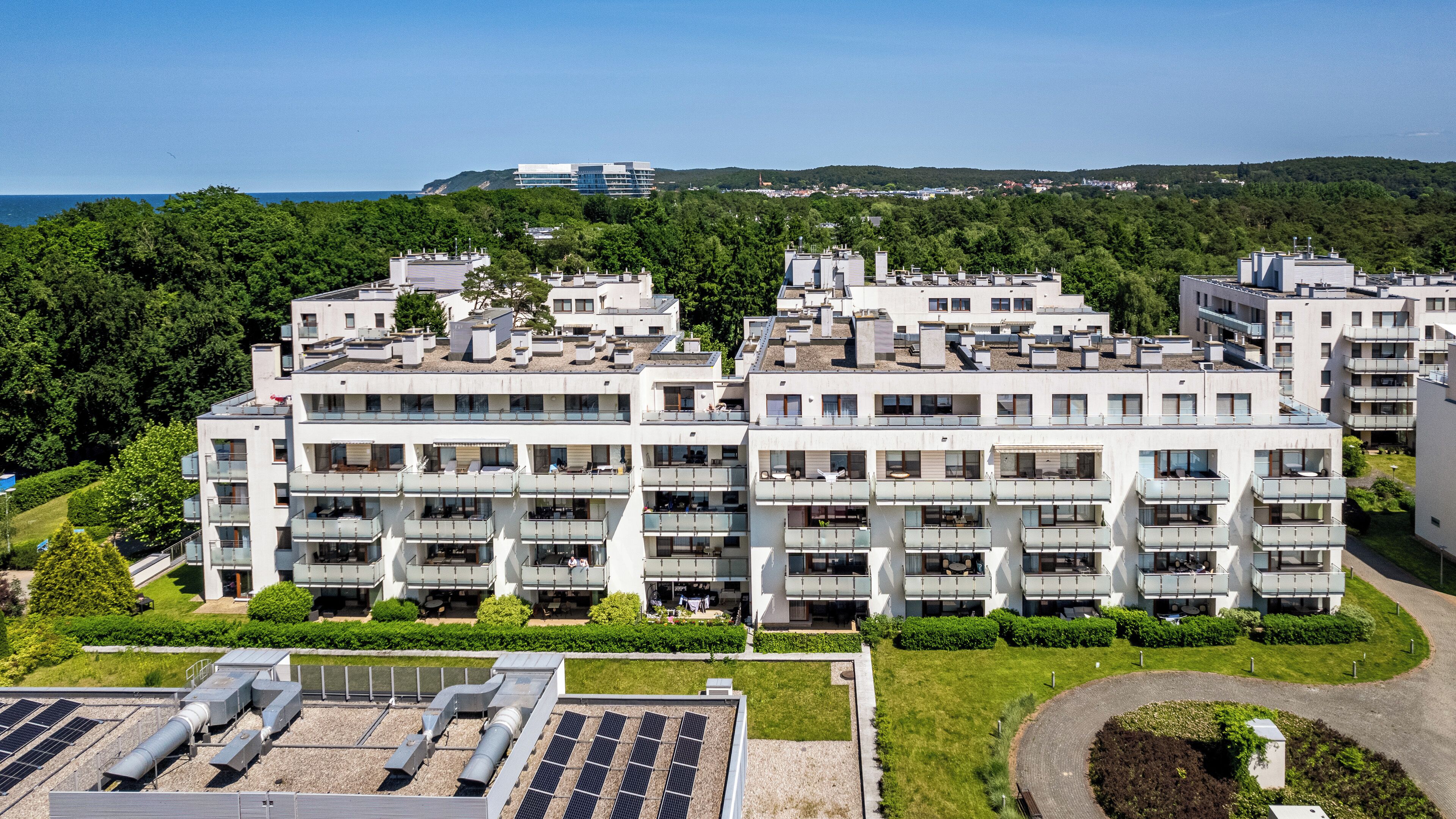 Un moderno edificio de apartamentos con varios balcones, paneles solares en el techo y vista al mar.