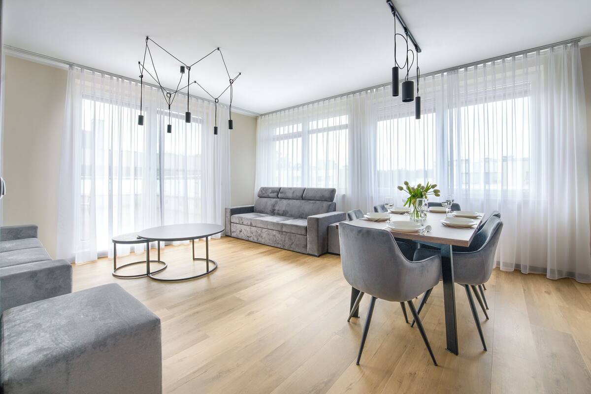 A modern living room with a grey sofa, a dining table set for four, and a grey accent chair.