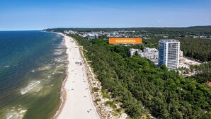 A coastal cityscape with a beach, dense forest, and modern buildings. - Apartamenty Sun & Snow Aquamarina (Miedzyzdroje)