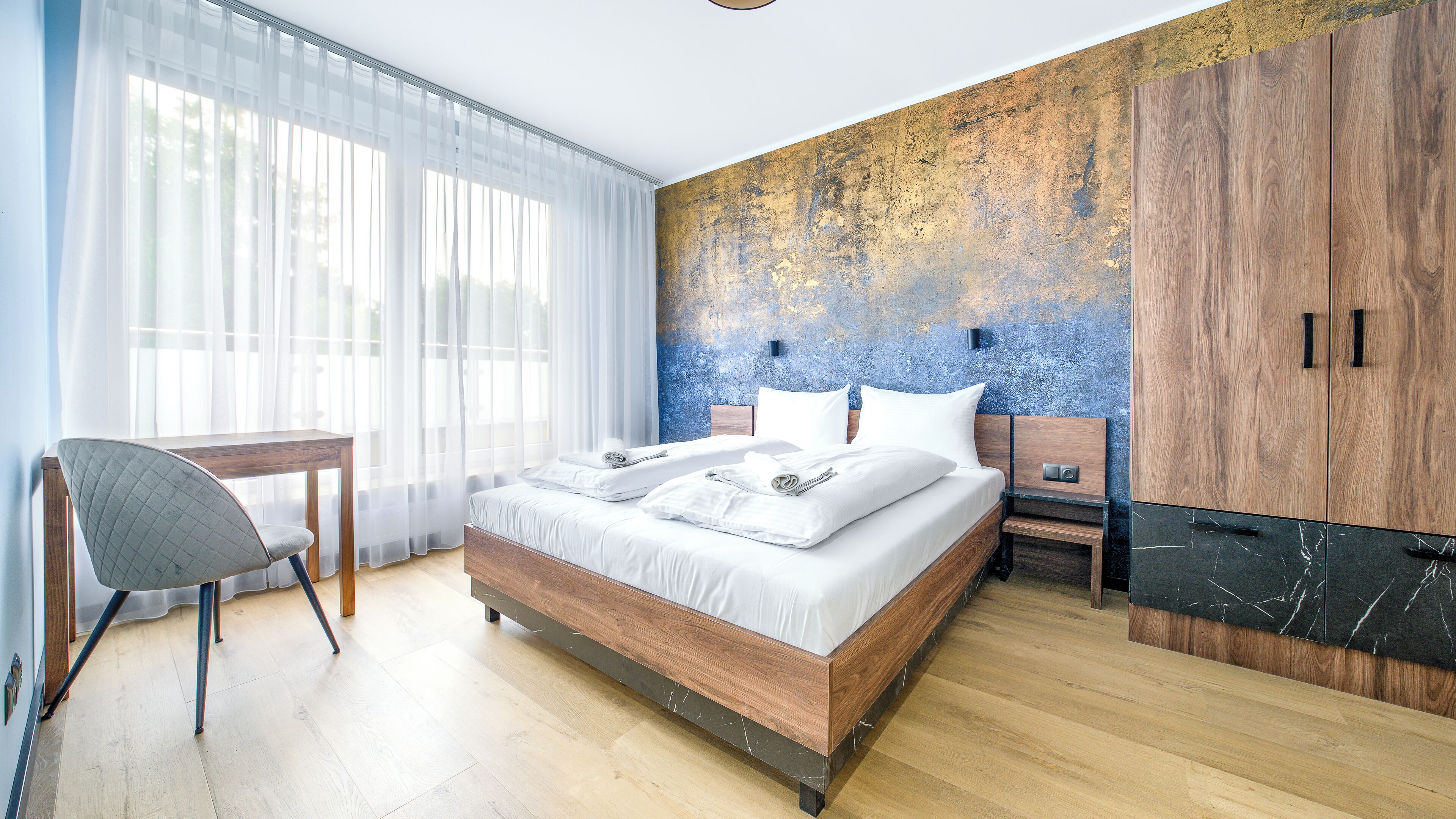 Una habitación de hotel moderna con una cama de madera, un escritorio y un armario grande.