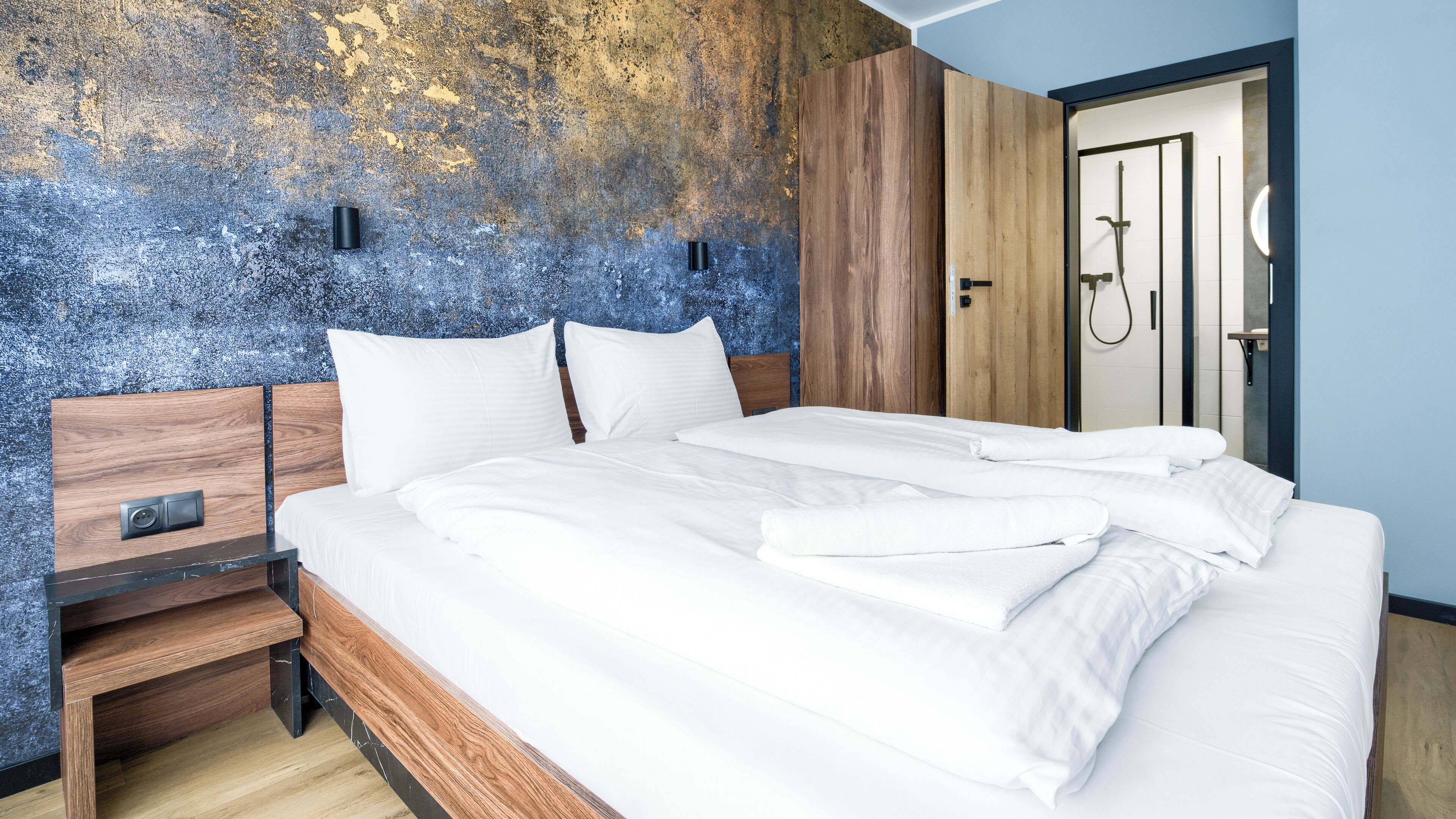A modern hotel room with a large bed, wooden headboard, and a textured wall.