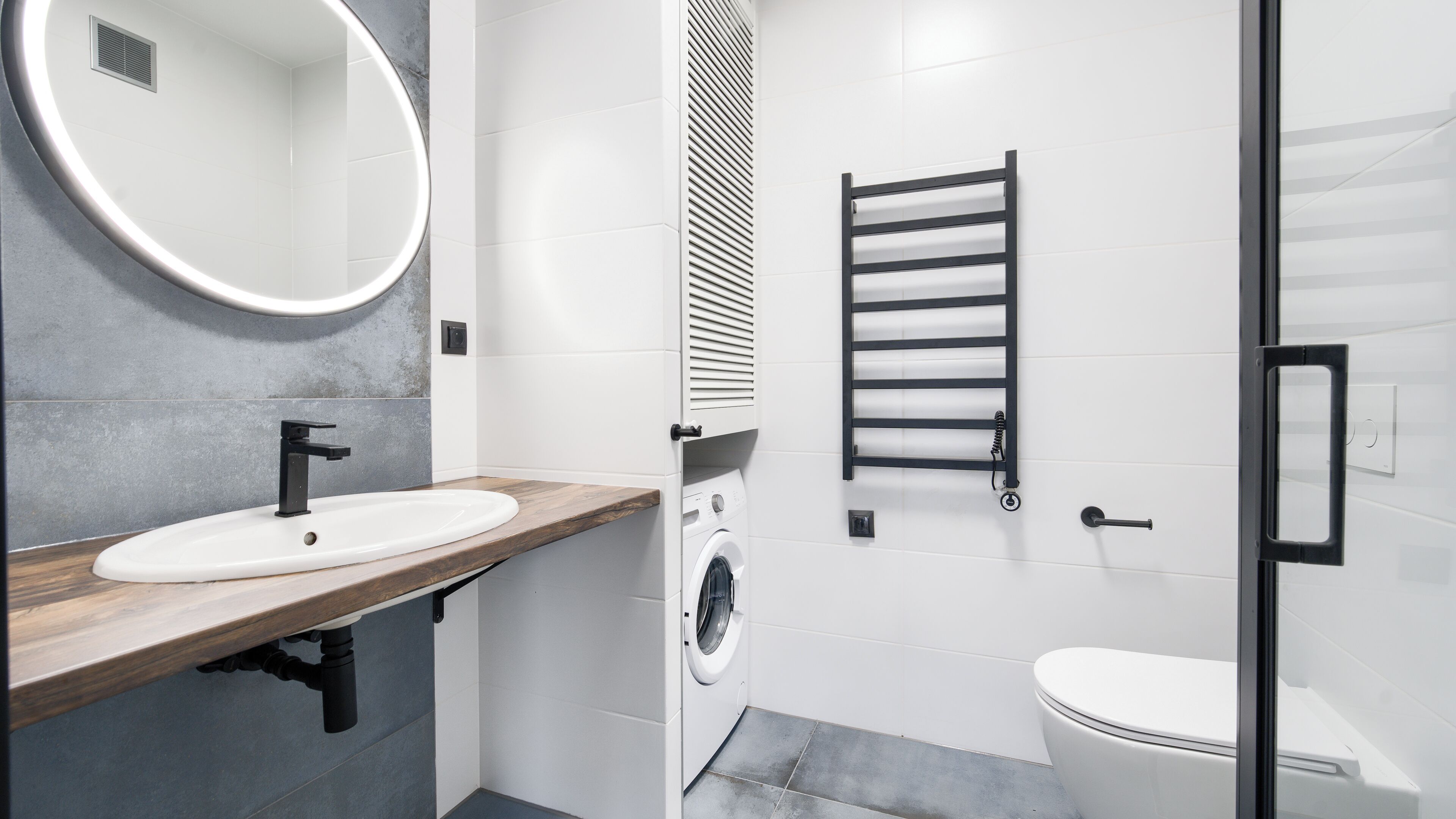 A modern bathroom with a wooden vanity, a washing machine, a towel rack, and a toilet.