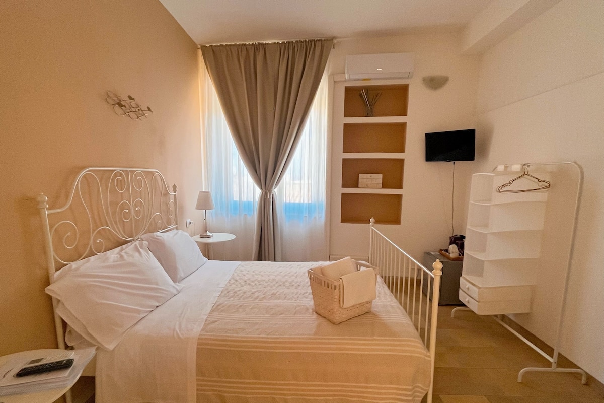 Een netjes ingerichte hotelkamer met een bed, nachtkastje, lamp, airconditioning, televisie en een kledingkast.
