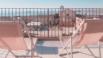 Un balcon avec deux fauteuils blancs, une vue sur la mer et un bâtiment doté d’un clocher.