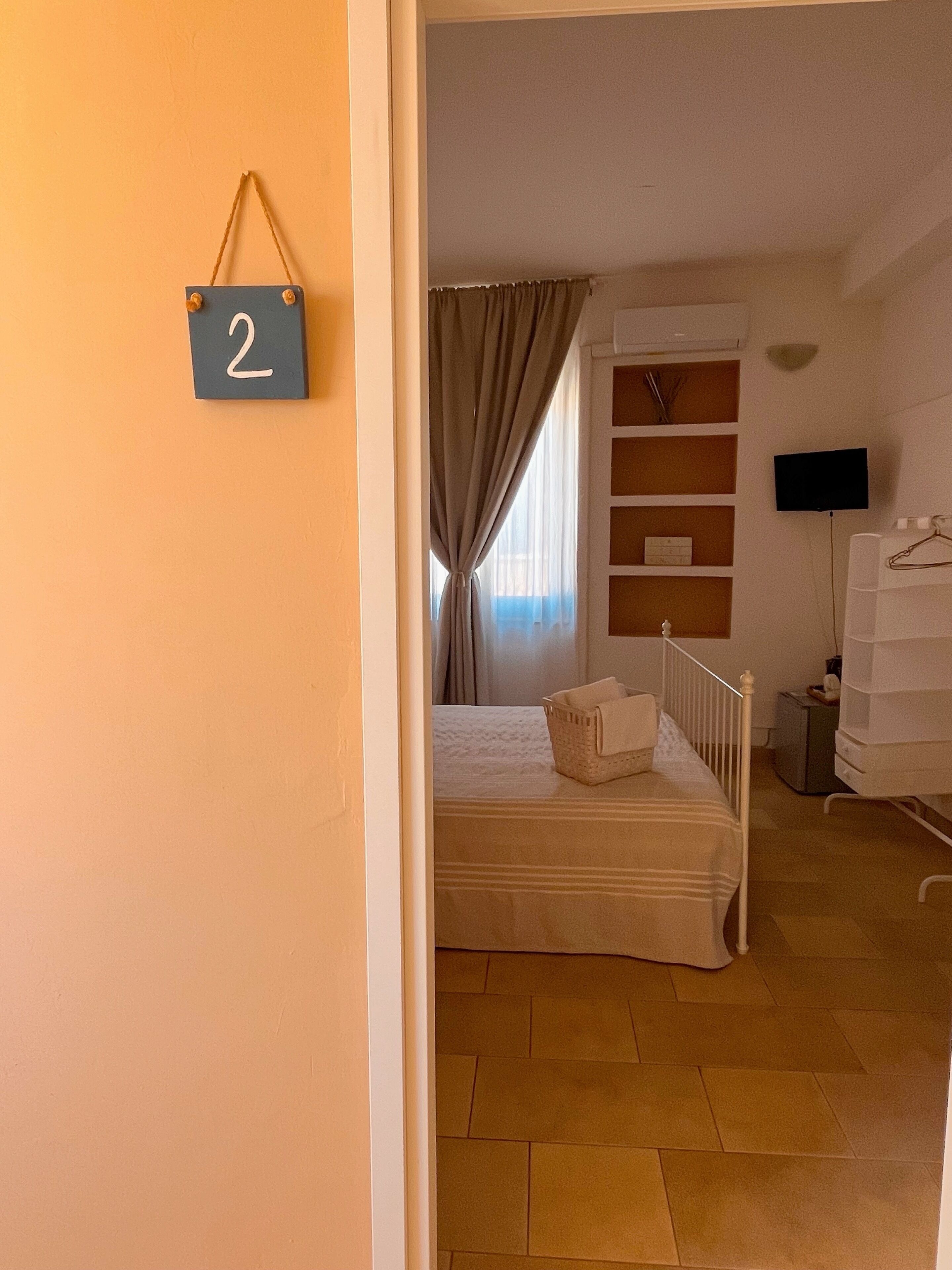 Quarto com cama, televisão, cómoda e prateleira com caixas organizadoras.