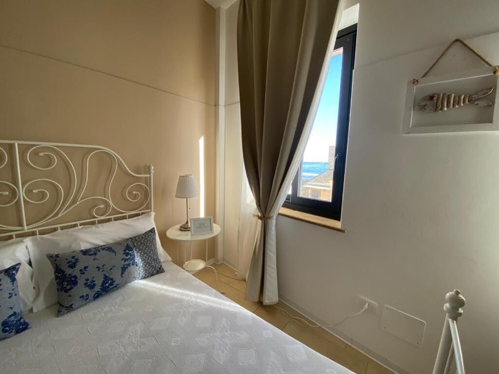 Ein Hotelzimmer mit einem Bett, einem Nachttisch, einer Lampe, einem Fenster mit Vorhängen und einem an der Wand befestigten Regal mit Dekoration.
