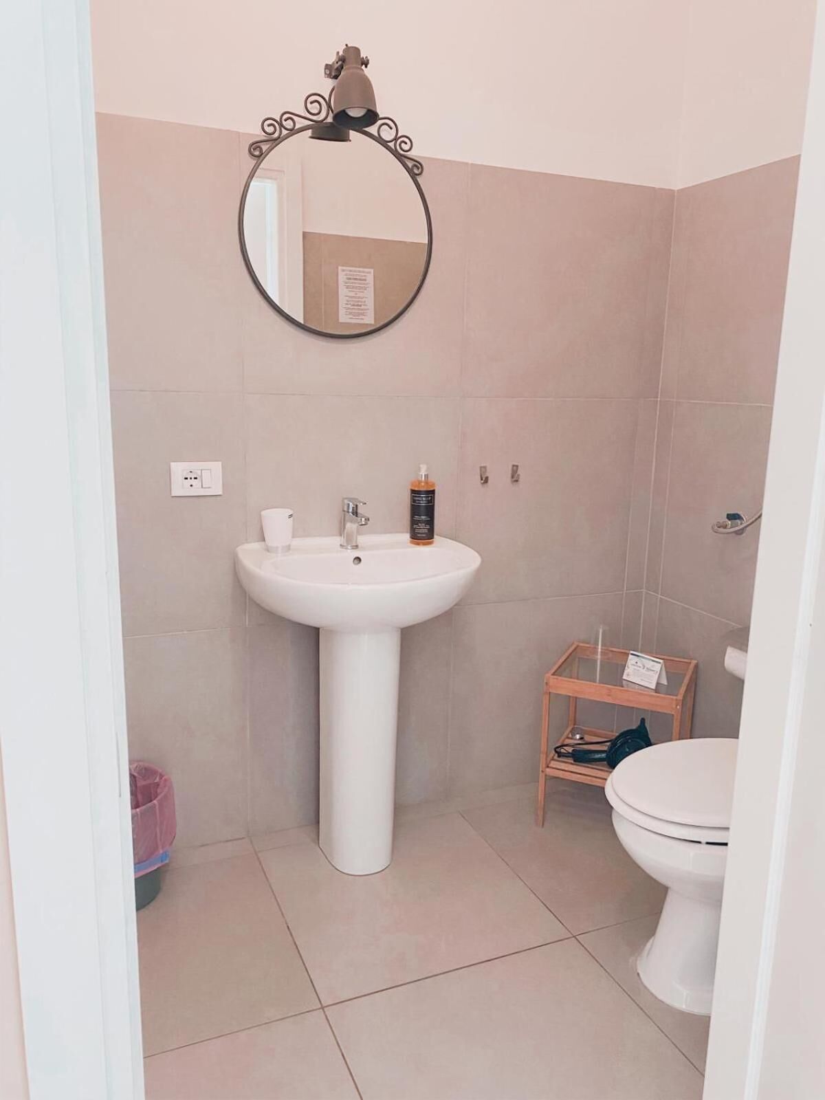 A bathroom with a pedestal sink, a mirror, a small wooden stool, and a toilet.
