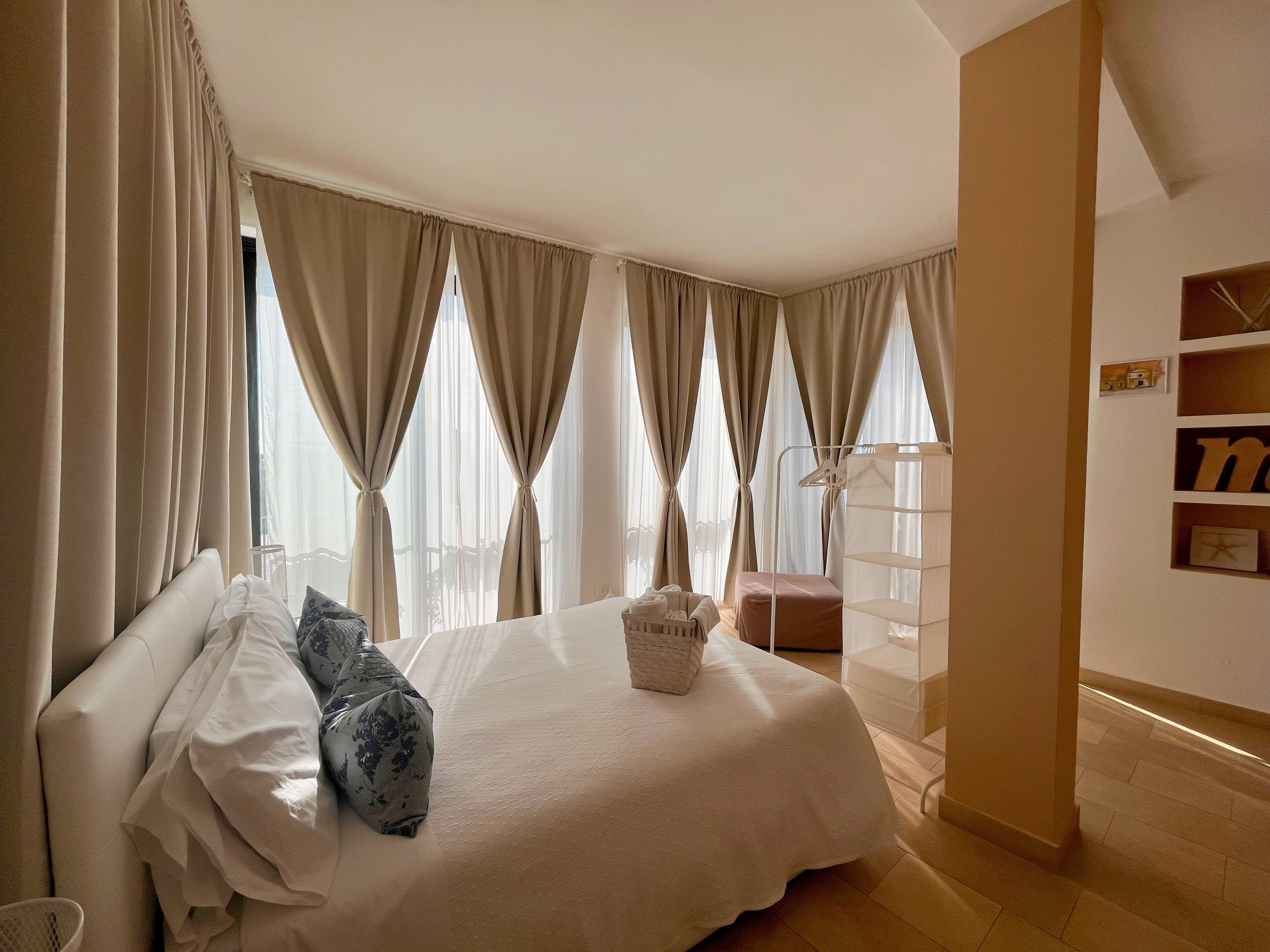 Una habitación de hotel con una cama grande, cortinas color beige, una mesita de noche y una pequeña zona de estar.