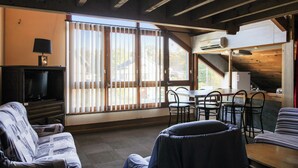 Een gezellige woonkamer met een bank, een televisie en een eethoek met stoelen en een tafel.