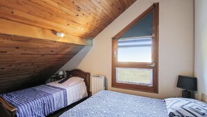 Een slaapkamer met twee bedden, houten balken in het plafond, een raam en een radiator.