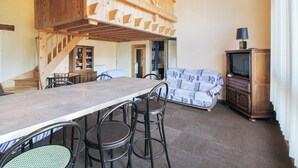 Een eetgedeelte met een hoog houten plafond, een lange tafel met stoelen, een bank en een televisie op een houten kast.