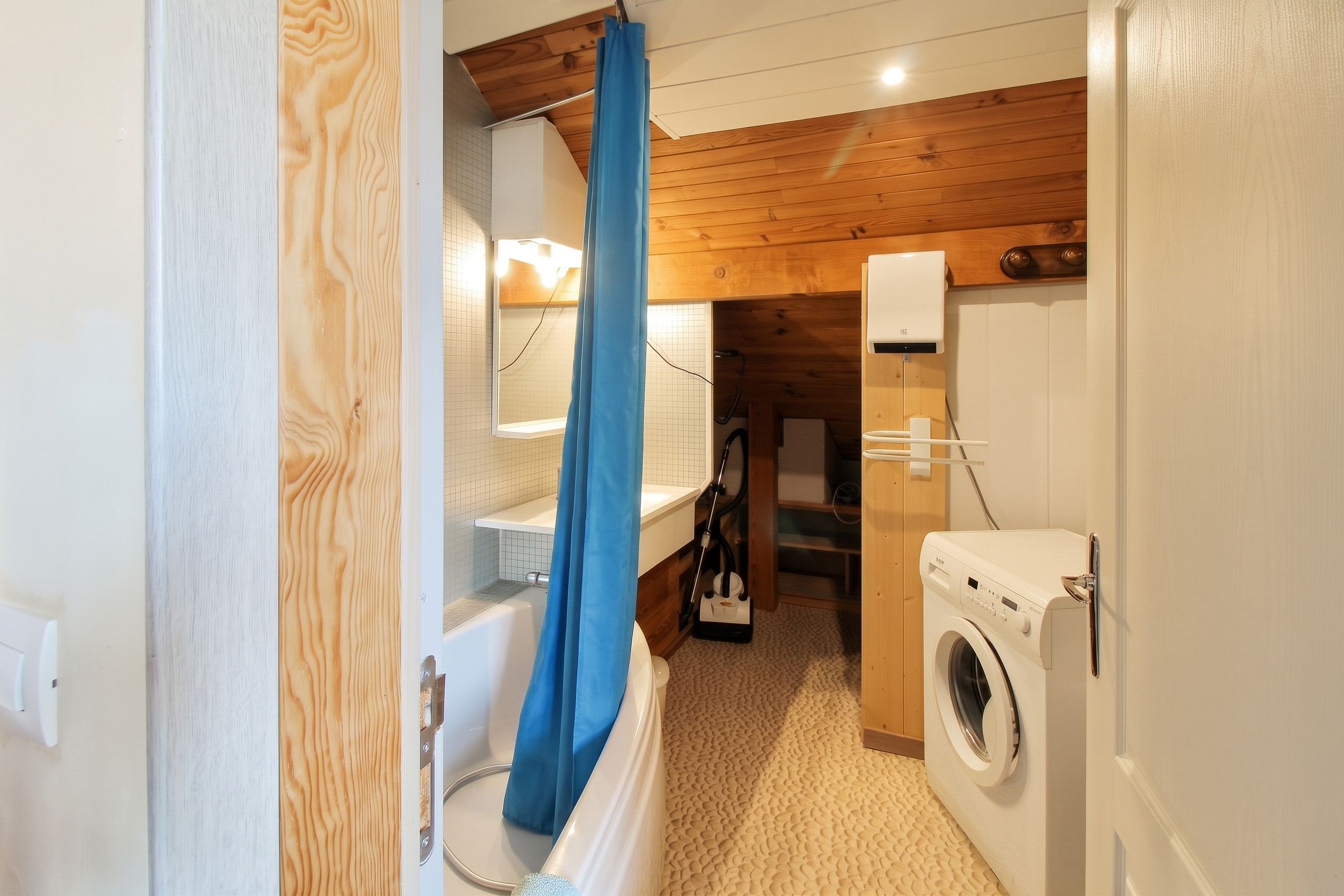 Une petite salle de bain comprenant une baignoire, un rideau de douche, un lave-linge et des toilettes.