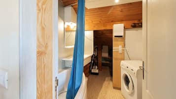 Une petite salle de bain comprenant une baignoire, un rideau de douche, un lave-linge et des toilettes.