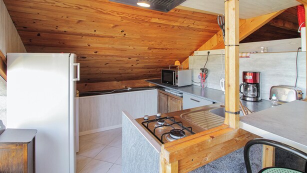 Een keuken met houten balken in het plafond, een gasfornuis, een magnetron en een koelkast.