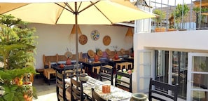 An outdoor dining area with multiple tables and chairs, a large umbrella, and decorative wall art.