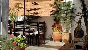 An outdoor patio with tables and chairs, surrounded by potted plants and a thatched roof. - Riad Art House (El Jadida)