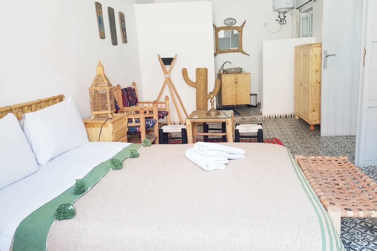 A bedroom with a bed, a wooden dresser, a small table, and a chair.