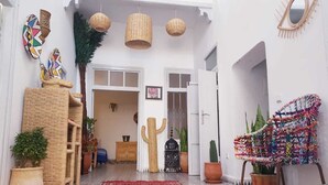 A spacious entrance with a red patterned rug, wicker furniture, and potted plants. - Riad Art House (El Jadida)