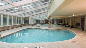 En indendørs swimmingpool med et glasloft, stengulv og et loungeområde med stole og borde.