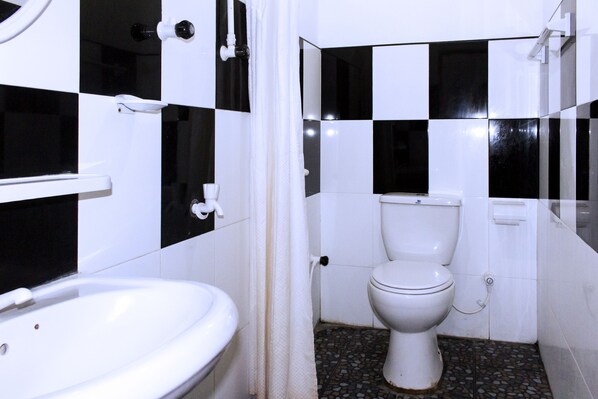 Un baño con un lavamanos blanco, un inodoro y una zona de ducha. Las paredes están cubiertas de un mosaico a cuadros blancos y negros.