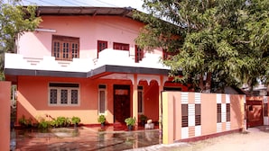 A two-story house with a red and white exterior, a front porch with potted plants, and a gated entrance. - D'Villa Guest House (Jaffna)