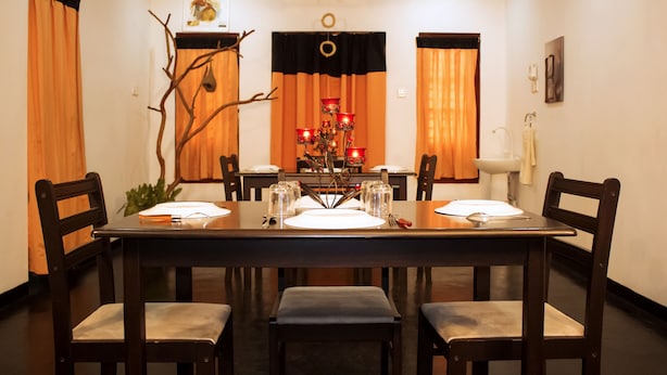 A dining room with a rectangular table set for four, surrounded by chairs. There is a chandelier in the center, and the room has a ceiling fan. - D'Villa Guest House (Jaffna)