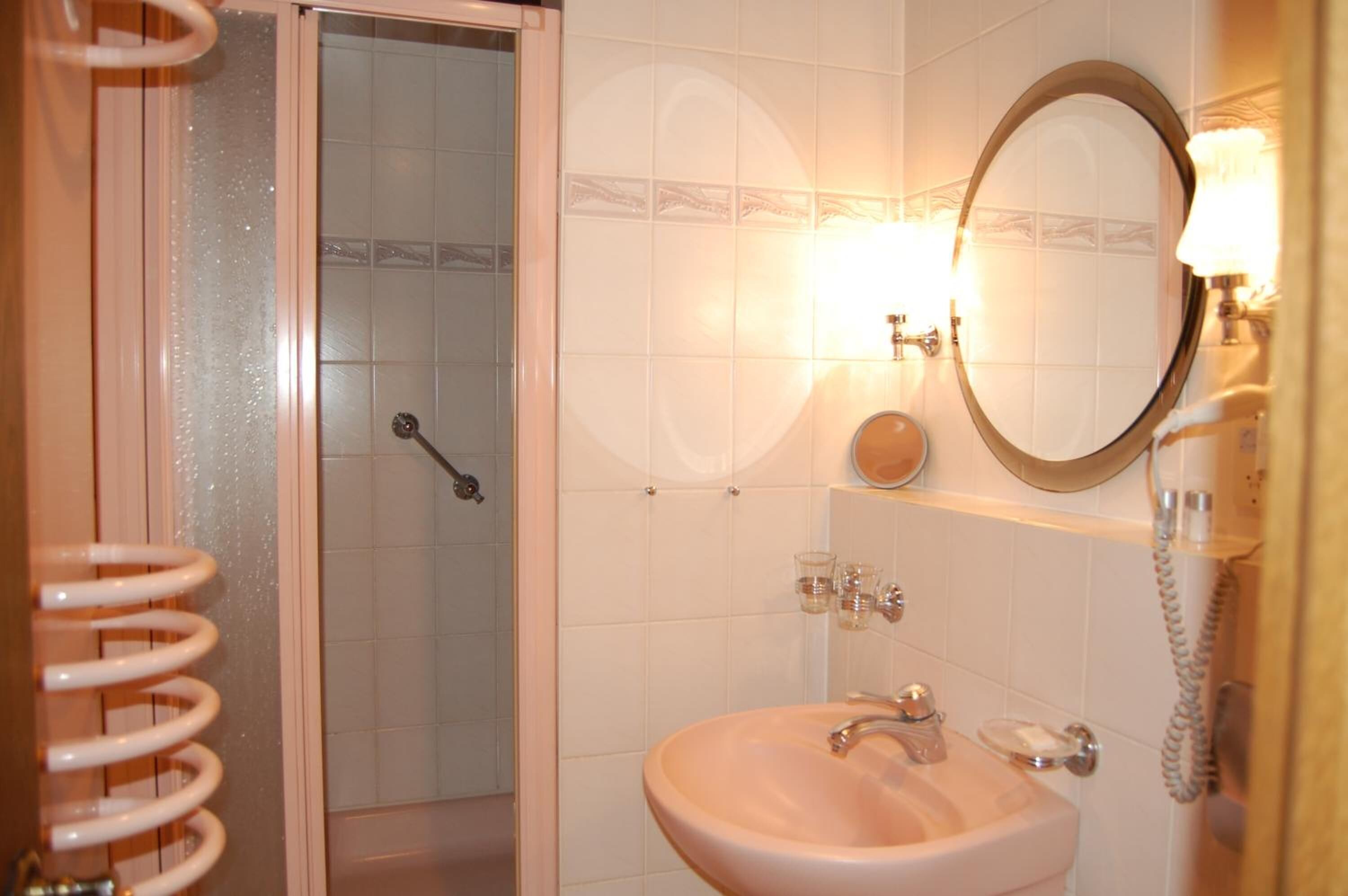 A bathroom with a shower, a sink, a mirror, and a telephone.