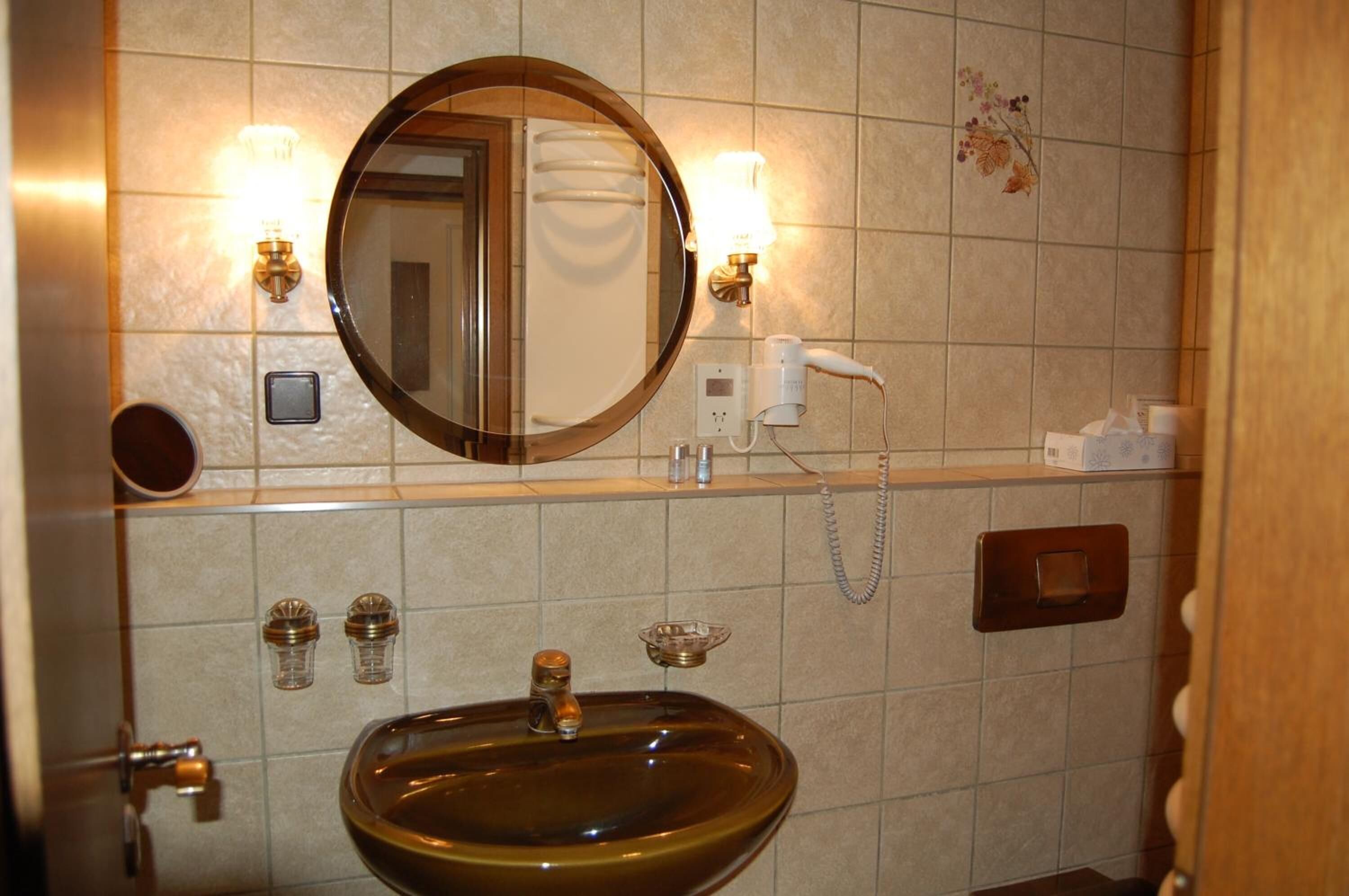 Ein Badezimmer mit rundem Spiegel, zwei Wandleuchten, einem Fön, einem Waschbecken und einem Handtuchhalter.